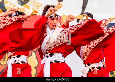 Japanische Teenager-Frau Yosakoi-Tänzerin in rotem, langärmligen Yukata tanzt auf der Bühne mit Naruko, Holzklatschen, im Kyusyu Gassai in Kumamoto. Stockfoto