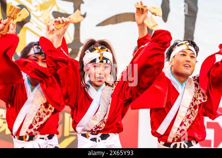 Japanische Teenager-Frau Yosakoi-Tänzerin in rotem, langärmligen Yukata tanzt auf der Bühne mit Naruko, Holzklatschen, im Kyusyu Gassai in Kumamoto. Stockfoto