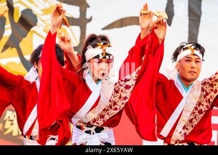 Japanische Teenager-Frau Yosakoi-Tänzerin in rotem, langärmligen Yukata tanzt auf der Bühne mit Naruko, Holzklatschen, im Kyusyu Gassai in Kumamoto. Stockfoto