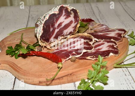Auf dem Tisch auf dem Schneidebrett befindet sich ein Stück geräucherten coppa-Käse und daraus geschnittene Scheiben. Stockfoto