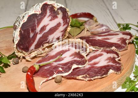 Geschnittenes rohes, geräuchertes Coppa-Fleisch liegt auf einem Schneidebrett. Stockfoto