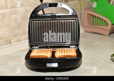 Der elektrische Grill ist geöffnet. Geröstetes Brot und Toast liegen auf der gerippten Oberfläche des Grills. Stockfoto