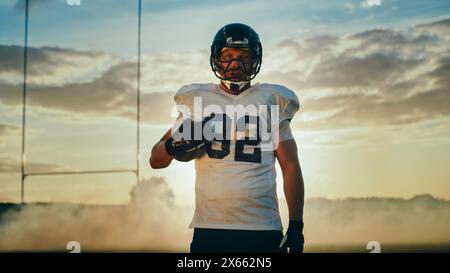 American Football Championship Game: Porträt eines muskulösen Spielers mit Helm und Ball. Profi-Athlet will gewinnen. Mächtig, Geschick, Anstrengung, Sieg. Stockfoto