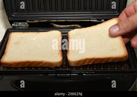 Auf dem Foto legt die Hand eines Mannes Toast auf die elektrische Grillplatte. Stockfoto