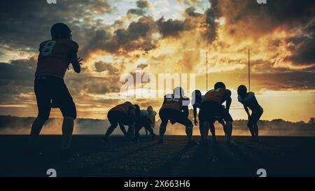 American Football Field zwei Teams stehen einander gegenüber und sind bereit, das Spiel zu starten. Professionelle Athleten bereiten sich auf den Ball vor, greifen an und kämpfen um den Sieg. Dramatische Golden Hour-Aufnahme Stockfoto