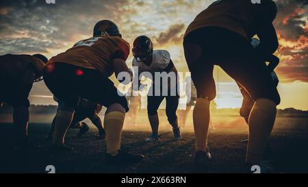 American Football Field zwei Teams stehen einander gegenüber und sind bereit, das Spiel zu starten. Professionelle Athleten bereiten sich auf den Ball vor, greifen an und kämpfen um den Sieg. Dramatische Golden Hour-Aufnahme Stockfoto