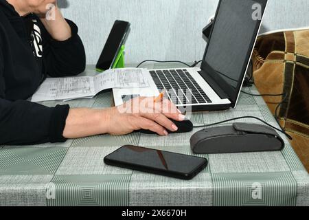 Eine Frau sitzt an einem Tisch vor einem Laptop-Bildschirm. Ihre Hand, mit einem Bleistift zwischen den Fingern, liegt auf der Computermaus. Stockfoto