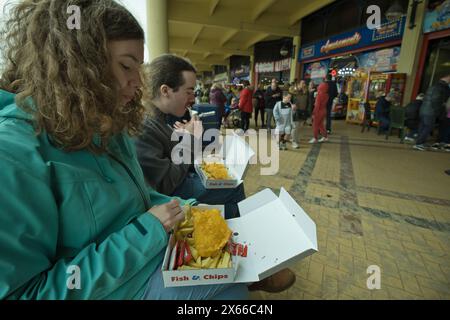 Junge Erwachsene essen Fish and Chips am Whitmore Bay Beach auf Barry Island in Wales im Frühjahr Stockfoto