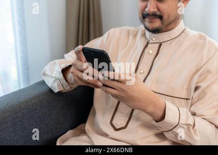 Der asiatische muslimische Mann benutzt zu Hause das Telefon. Stockfoto