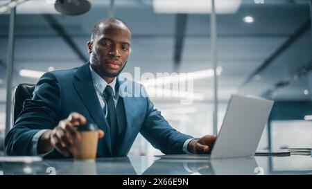 Top Management Modern Office: Erfolgreicher schwarzer Geschäftsmann in maßgeschneidertem Anzug, der an einem Laptop arbeitet. Professioneller afroamerikanischer CEO für die Verwaltung von Aktienkonten für Investmentkunden Stockfoto