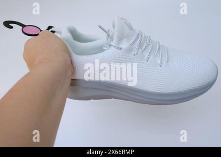 Weibliche Hände mit neuen weißen Trekkingschuhen, gebunden mit Schnürsenkeln auf hellem Hintergrund, Concept Schuhpflege und -Pflege, Fitness und Sport, Active Life Stockfoto