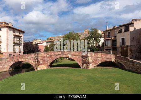 Eine Steinbrücke überspannt einen grünen Bereich und verbindet malerische Häuser unter einem teilweise bewölkten Himmel in einer historischen Umgebung Stockfoto