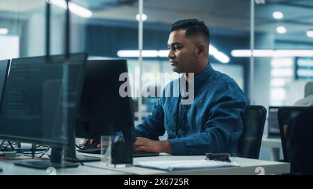 In diverse Office: Porträt eines hübschen Indianers, der am Desktop-Computer arbeitet. Focus Professional Entwickelt Innovative Software Und Modernes App-Design. Eleganter, Authentischer Multi-Ethnic-Arbeitsplatz Stockfoto
