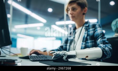 Vielfältiges Body positive Office: Porträt einer motivierten Frau mit Behinderung mit Hilfe einer Armprothese am Computer. Profi mit futuristischer, gedankengesteuerter myoelektrischer Bionik-Hand Stockfoto