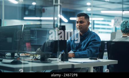 In diverse Office: Porträt eines hübschen Indianers, der am Desktop-Computer arbeitet. Professioneller Programmierer Entwickelt Innovative Software Und Modernes App-Design. Eleganter, Authentischer Multi-Ethnic-Arbeitsplatz Stockfoto