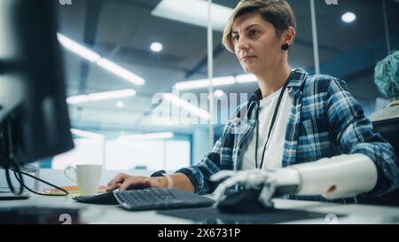 Vielfältiges Body positive Office: Porträt einer motivierten Frau mit Behinderung mit Hilfe einer Armprothese am Computer. Tapferer Profi mit futuristischer, gedankengesteuerter myoelektrischer bionischer Hand Stockfoto