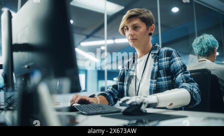 Vielfältiges Body positive Office: Porträt einer motivierten Frau mit Behinderung mit Hilfe einer Armprothese am Computer. Tapferer Profi mit futuristischer, gedankengesteuerter myoelektrischer bionischer Hand Stockfoto