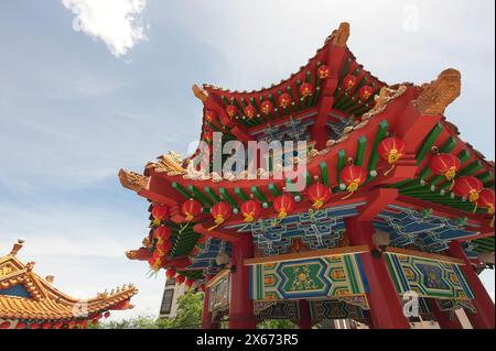 Lebendiges Bild einer goldenen Drachenskulptur auf einem traditionellen chinesischen Gebäudedach, das mit roten Laternen vor einem klaren blauen Himmel geschmückt ist. Stockfoto