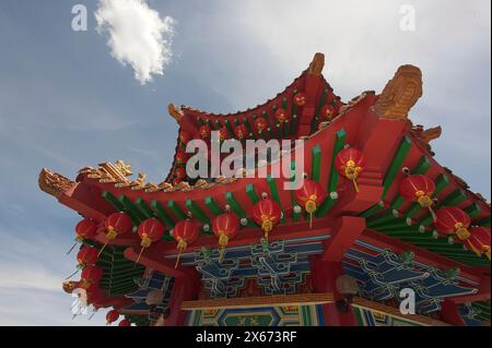 Lebendiges Bild einer goldenen Drachenskulptur auf einem traditionellen chinesischen Gebäudedach, das mit roten Laternen vor einem klaren blauen Himmel geschmückt ist. Stockfoto