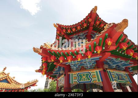 Lebendiges Bild einer goldenen Drachenskulptur auf einem traditionellen chinesischen Gebäudedach, das mit roten Laternen vor einem klaren blauen Himmel geschmückt ist. Stockfoto