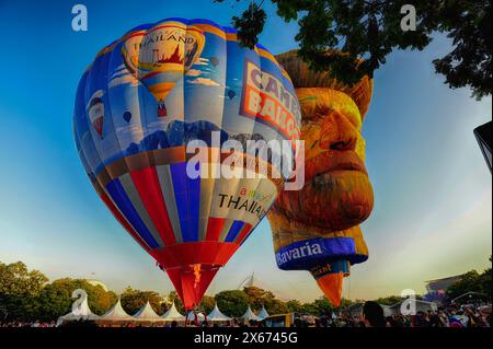 Zwei Heißluftballons schweben am Himmel, von denen einer wie das Gesicht eines Mannes geformt ist. Der andere Ballon ist wie ein riesiger Bär geformt. Die Szene ist li Stockfoto