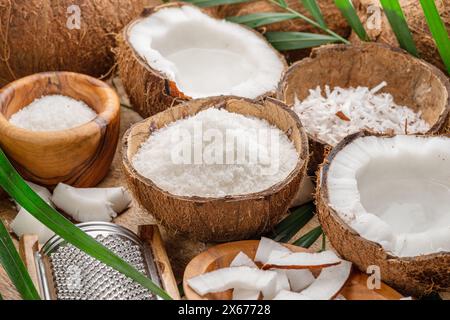 Frisch geöffnete Kokosnüsse zusammen mit Kokosscheiben, Flocken und Kokosblättern auf einem Holztisch. Schöner Hintergrund für Ihre Projekte. Stockfoto