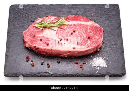 Rohes Ribeye-Steak mit Pfefferkörnern und Rosmarin auf Graphitservierbrett isoliert auf weißem Hintergrund. Stockfoto