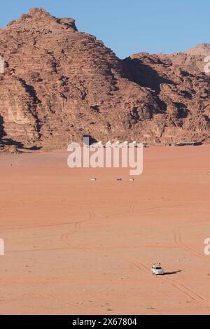 Wadi Rum, Jordanien - Fahrzeug mit Allradantrieb überquert die weite abgelegene Wüste mit luxuriösem Touristencamp im Hintergrund - Foto August 2023 Stockfoto