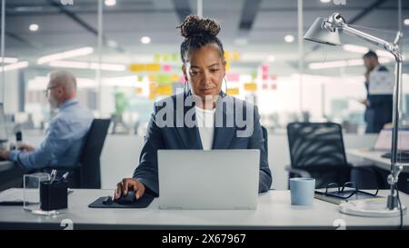 Porträt einer glücklichen afroamerikanischen Geschäftsfrau mit Laptop-Computer im modernen Büro. Stilvoller, schöner Manager, der an Finanz- und Marketingprojekten arbeitet. Stockfoto