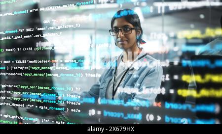 Diverse Büros: Porträt eines selbstbewussten indischen IT-Programmierers, der auf Desktop-Computern arbeitet. Professionelle Spezialistin Für Frauen Entwickelt Innovative Software. Aufgenommen mit visuellen Effekten von Running Code. Stockfoto