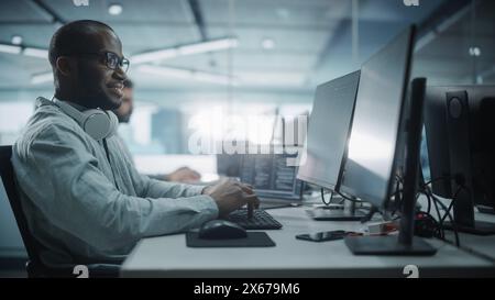 Authentic Office: Porträt des Black IT Programmierers, der auf einem Desktop-Computer arbeitet. Männliche Website, Software Engineer Entwickelt App, Programm, Videospiel. Stilvolle Seitenansicht Stockfoto