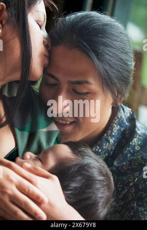 Ein herzerwärmender Moment eines ecuadorianischen Vaters, der sein neugeborenes Baby hält, während sein Partner ihm einen liebevollen Kuss gab und eine zarte Familienszene zeigt Stockfoto