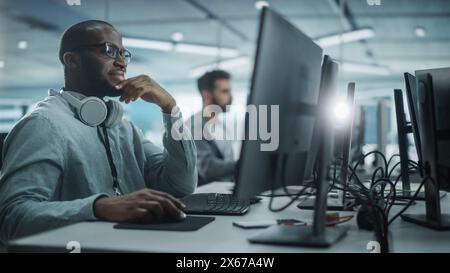 Authentic Office: Motivierter Black IT Programmierer, der auf einem Desktop-Computer arbeitet. Männliche Website, Software Engineer Entwickelt App, Programm, Videospiel. Terminal mit Codierungssprache. Stockfoto