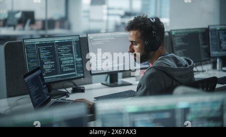 Büro: Professional White IT Programmer verwendet Kopfhörer, während er auf einem Desktop-Computer arbeitet. Männlicher Websiteentwickler, Software Engineer, Der App Entwickelt, Videospiel. Podcast hören, Musik. Stockfoto