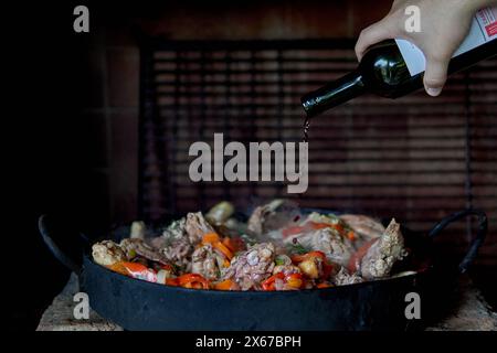 Die Hand des Mannes, der Rotwein über Pollo al Disco gießt und auf einer Pflugscheibe in Argentinien gekocht wird Stockfoto