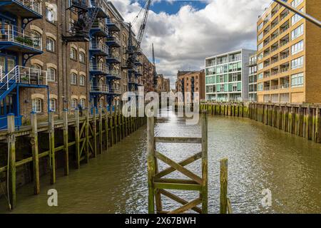 Altes historisches Lagerhaus, das heute in Wohngebäude umgebaut wurde, grenzt an die Themse mit grünem Schlamm und Moos von Ebbe in den Docklands in London. Stockfoto