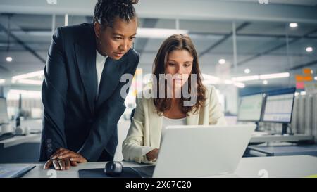 Zwei weibliche Kollegen diskutieren liebevoll über die Arbeit, lächeln, während sie Project on Laptop in diversen modernen Geschäftsbüros zeigen. Erfahrener Manager und junger Mitarbeiter diskutieren analytische Daten. Stockfoto