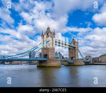 Panoramablick auf Londons Tower Bridge von der Themse aus mit Seeverkehr und Fähren, die unter blauem Himmel mit weißem cl entlang des Flusses segeln Stockfoto