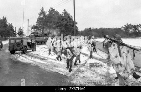 Wintermanöver, Reforger 1985, Zentralwächter, im Raum Kassel, Homberg/Efze, Neukirchen, Schwalmstadt, Vogelsberg, Frankenberg (Januar - Februar 1985), US-Soldaten, die die Straße mit weißen Umhängen als Tarnung überqueren, begleitet von Jeeps und gepanzerten Fahrzeugen Stockfoto