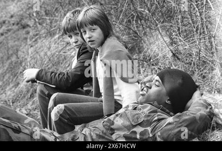 Wintermanöver, Reforger 1985, Zentralwächter, im Raum Kassel, Homberg/Efze, Neukirchen, Schwalmstadt, Vogelsberg, Frankenberg (Jan. - Feb. 1985), US-Soldat macht eine Pause, legt sich auf den Straßendamm, die beiden Gesellen schließen sich ihm an Stockfoto