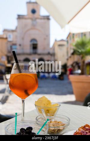 Porträt eines Aperol Spritz mit Kartoffelchips (Aperitivo), imposante Gebäude der Altstadt von Tropea im Hintergrund Stockfoto