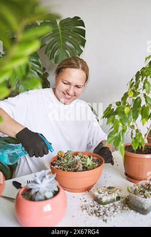 In einem gemütlichen Zimmer pflegt eine lächelnde Frau mit Sorgfalt ihre geliebten Pflanzen und schafft eine grüne Oase in ihrem Zuhause. Ihr fröhliches Auftreten spiegelt ihre Liebe zum Gartenbau wider und macht den Balkon zu einem fröhlichen Oase Stockfoto