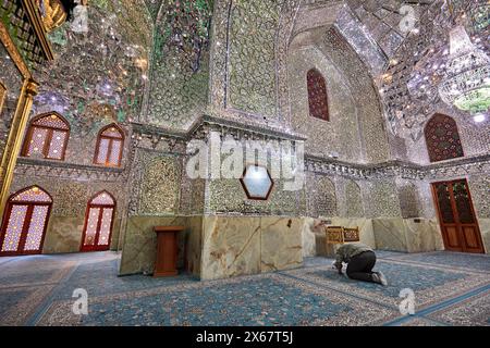 Ein Mann betet im Ali Ibn Hamzeh Heiligtum, das im Inneren aufwendig mit glänzenden Spiegelfliesen (aina-kari) verziert ist. Shiraz, Iran. Stockfoto