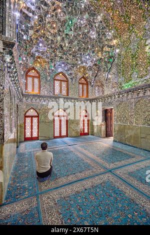 Ein Mann betet im Ali Ibn Hamzeh Heiligtum, das im Inneren aufwendig mit glänzenden Spiegelfliesen (aina-kari) verziert ist. Shiraz, Iran. Stockfoto