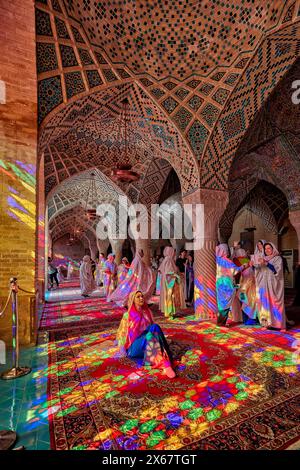 Eine Frau sitzt im Licht von bunten Buntglasfenstern in der Nasir al-Mulk Moschee aus dem 19. Jahrhundert, auch bekannt als die Rosa Moschee. Shiraz, Iran. Stockfoto