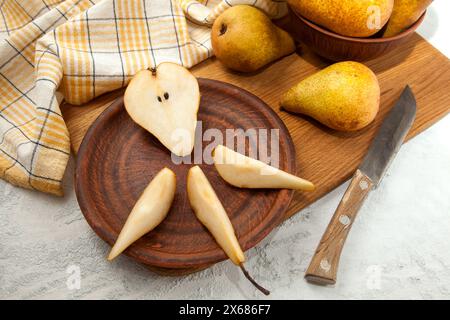 Tonplatte mit Scheiben und der Hälfte reifer saftiger Birnenfrüchte, Korbkorb mit Birnen und gelbes Küchentuch auf Holzschneidebrett. Stockfoto
