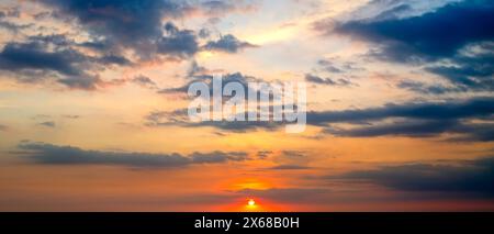 Heller Sonnenuntergang am blauen Himmel. Die Sonnenstrahlen strahlen strahlen durch die Wolken. Breites Foto . Stockfoto