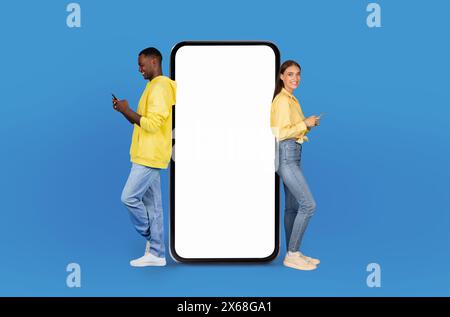 Junge Paare, die ihre Smartphones benutzen, getrennt durch den riesigen leeren Bildschirm Stockfoto