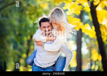 Love Story Verlobungssitzung eines glücklichen jungen kaukasischen hetero lächelnden Paares in weißen Pullis und blauen Jeans, das Mädchen umarmt ihren Freund A Stockfoto