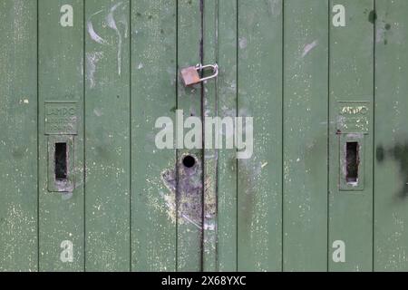 Alte baufällige Tür grün lackiert und mit einem Vorhängeschloss geschlossen Stockfoto